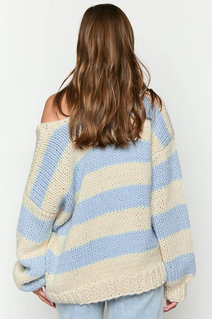 Blue - Woman wearing a chunky knit, slouchy off-shoulder jumper featuring wide horizontal stripes, paired with light wash denim jeans.