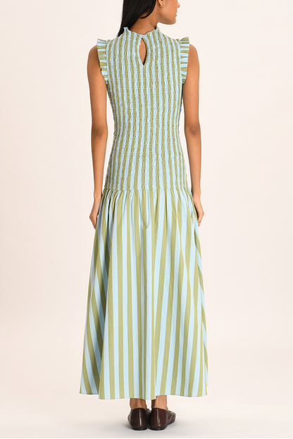 A woman models a sleeveless maxi dress with a high neckline and a fully smocked bodice. The dress features a pattern of vertical light blue and olive green stripes, ruffled shoulder details, and a full A-line skirt.