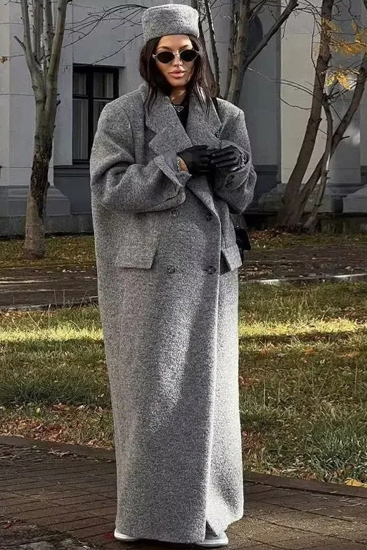 Grey - A woman wearing a long, oversized grey double-breasted maxi coat with wide lapels and flap pockets, styled for winter.