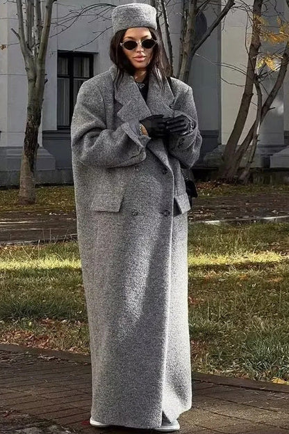 Grey - A woman wearing a long, oversized grey double-breasted maxi coat with wide lapels and flap pockets, styled for winter.