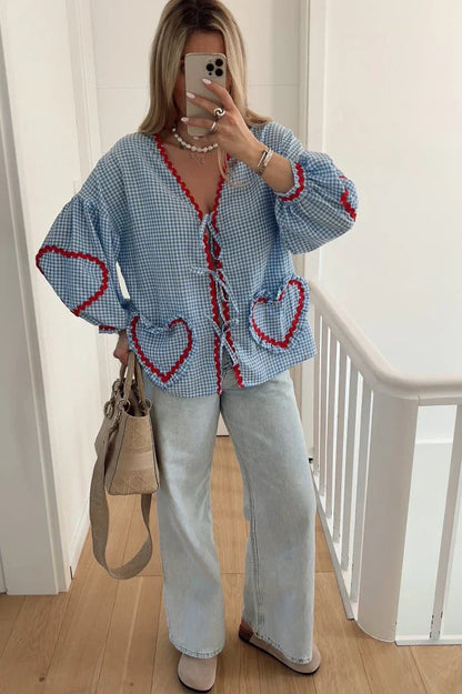 Blue - Women's pink and white gingham tie-front blouse featuring long sleeves, contrast red scalloped trim, and playful heart-shaped appliqués, styled with light wash denim shorts.