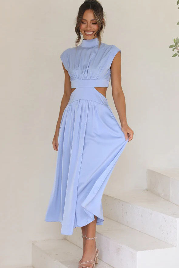 A woman walks outdoors in a pale yellow midi dress, its full skirt flowing around her. The dress features a high funnel neck, cap sleeves, and cutouts at the waist.