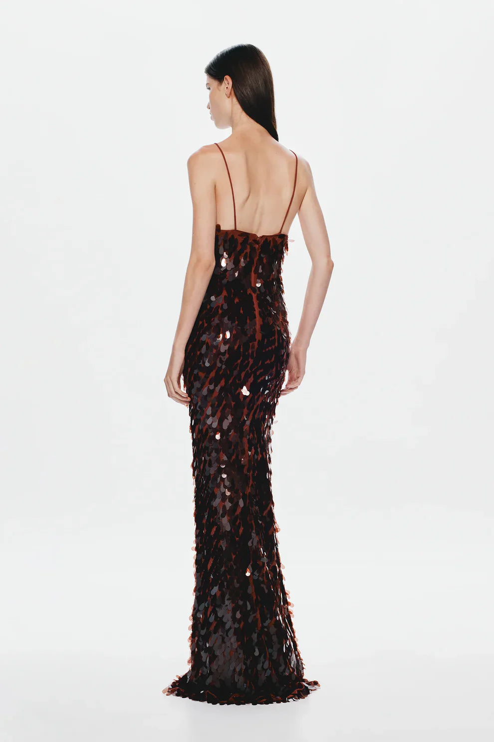 A woman models a floor-length, dark formal gown covered in large, reflective metallic teardrop sequins, featuring a deep plunging V-neckline and thin spaghetti straps against a plain white background.