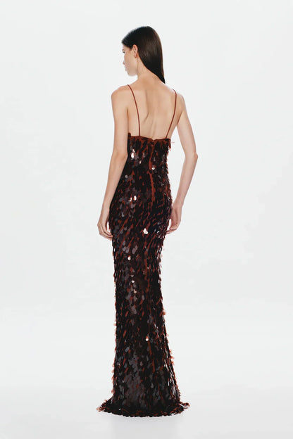 A woman models a floor-length, dark formal gown covered in large, reflective metallic teardrop sequins, featuring a deep plunging V-neckline and thin spaghetti straps against a plain white background.