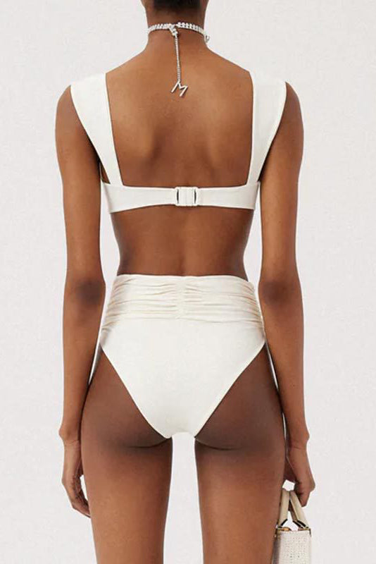 White - A woman models a structured, off-white two-piece bikini featuring a bandeau top with wide straps and high-waisted, high-cut bottoms adorned with a large, 3D rose appliqué at the waist.