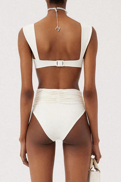 White - A woman models a structured, off-white two-piece bikini featuring a bandeau top with wide straps and high-waisted, high-cut bottoms adorned with a large, 3D rose appliqué at the waist.