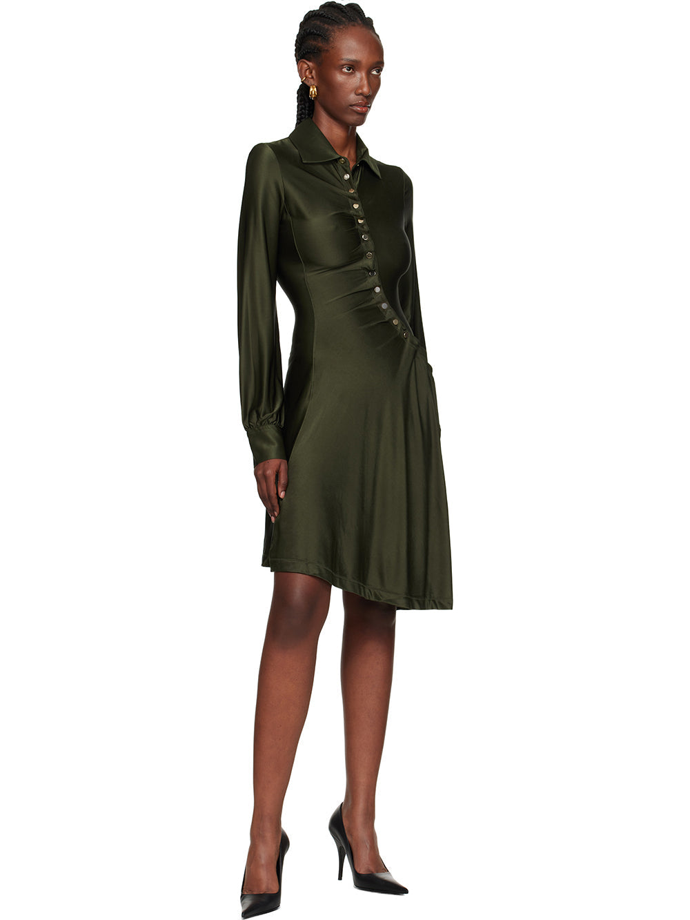 Black - Full-length view of a woman wearing a long-sleeved, knee-length shirt dress in a lustrous olive green, featuring an asymmetrical button front, ruched detailing, and an uneven hem.