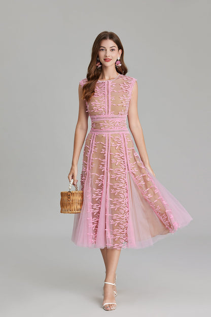 Full-length view of a woman wearing a sleeveless, sheer midi dress in pink and nude, featuring elaborate pink botanical embroidery in vertical panels and a flared tulle skirt.