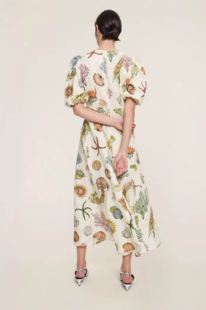 A woman models a short-sleeve, crewneck midi dress with a white background and a colorful, illustrative print of marine life including jellyfish, coral, and seashells.