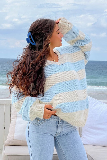 Blue - Woman wearing a chunky knit, slouchy off-shoulder jumper featuring wide horizontal stripes, paired with light wash denim jeans.