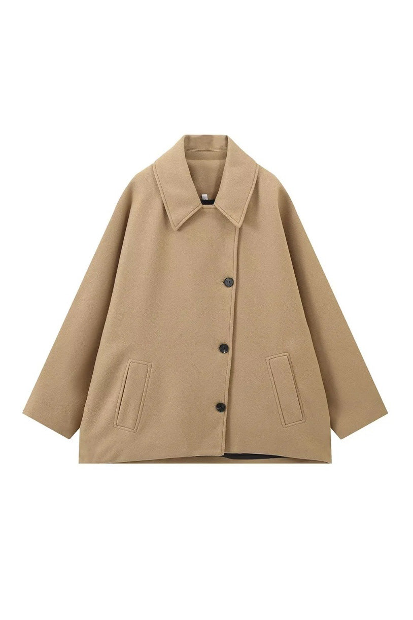 Khaki - A woman wearing a black oversized short coat with drop shoulders and a notched lapel, styled over a grey turtleneck and black shorts for a chic city look.
