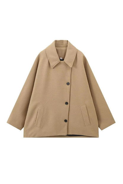 Khaki - A woman wearing a black oversized short coat with drop shoulders and a notched lapel, styled over a grey turtleneck and black shorts for a chic city look.
