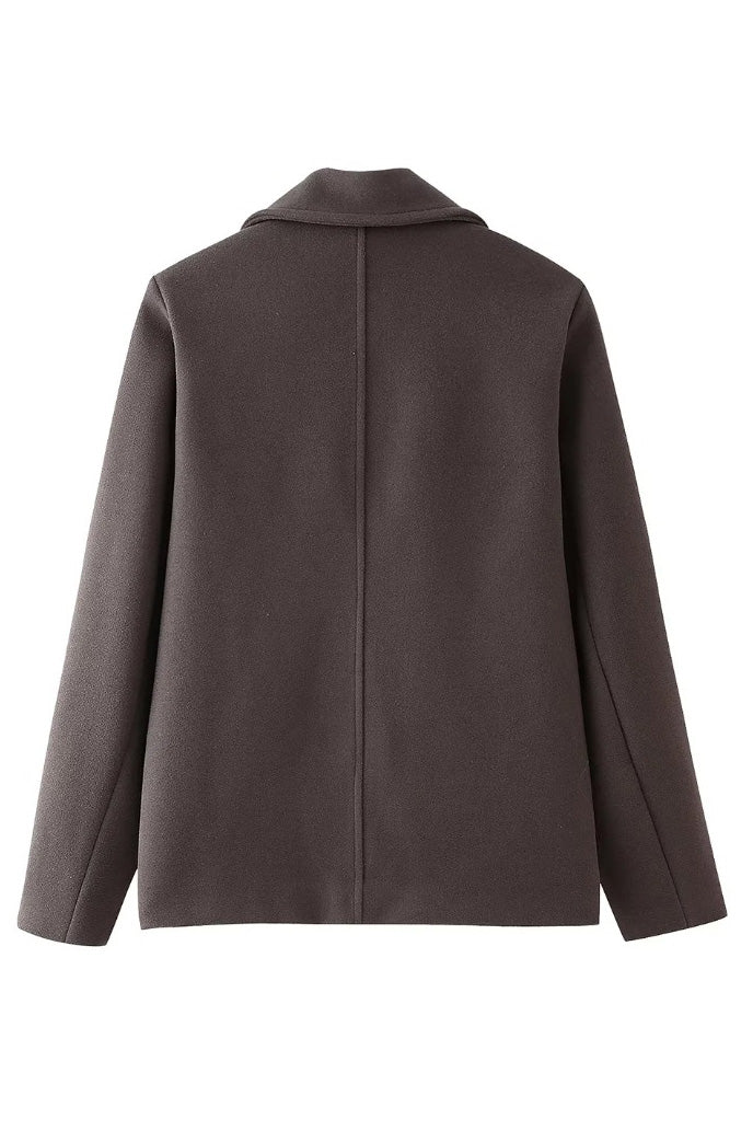 Grey - A woman wearing a taupe, short boxy jacket with oversized notch lapels, wide sleeves, and a double-breasted button front, styled over a black top.