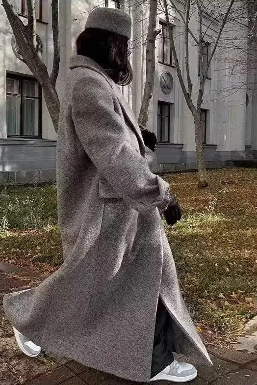 Grey - A woman wearing a long, oversized grey double-breasted maxi coat with wide lapels and flap pockets, styled for winter.