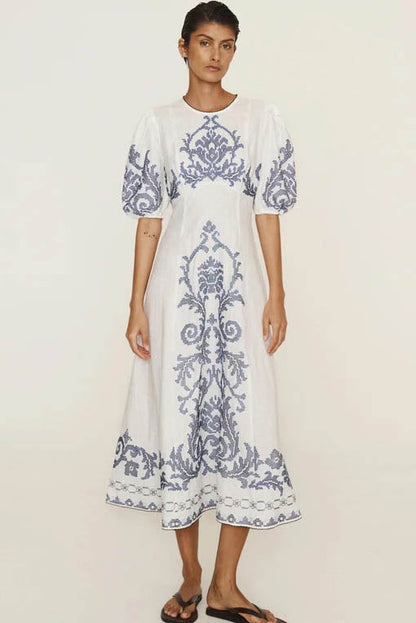 A woman models a short-sleeve, crewneck midi dress with a white background and a colorful, illustrative print of marine life including jellyfish, coral, and seashells.