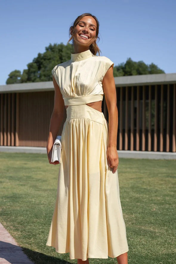 Yellow - A woman models a pale yellow, high-neck, sleeveless midi dress with a ruched bodice, a side waist cut-out, and a full, flowing A-line skirt, standing outdoors.