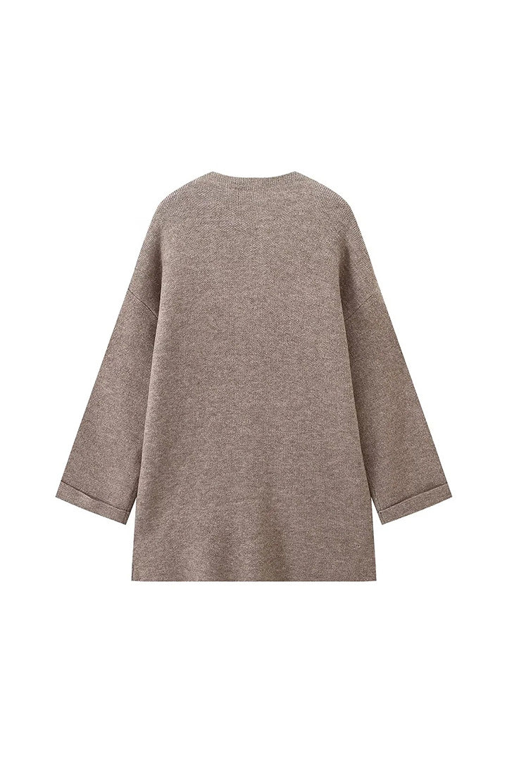 Grey - A woman wearing a thick, taupe oversized longline winter coat featuring a built-in scarf neckline, dark button closures, and large patch pockets.