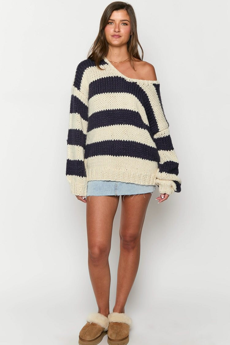 Black - Woman wearing a chunky knit, slouchy off-shoulder jumper featuring wide horizontal stripes, paired with light wash denim jeans.