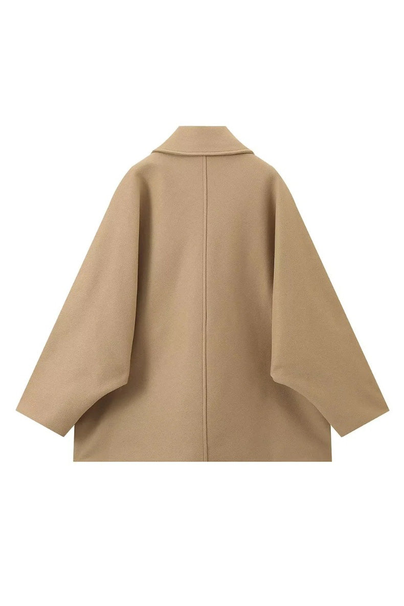 Khaki - A woman wearing a black oversized short coat with drop shoulders and a notched lapel, styled over a grey turtleneck and black shorts for a chic city look.