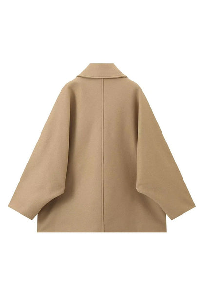 Khaki - A woman wearing a black oversized short coat with drop shoulders and a notched lapel, styled over a grey turtleneck and black shorts for a chic city look.