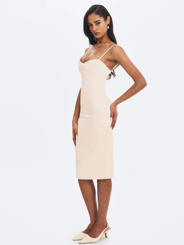 A woman modeling a fitted cream-colored midi dress with spaghetti straps and a ruched sweetheart neckline.