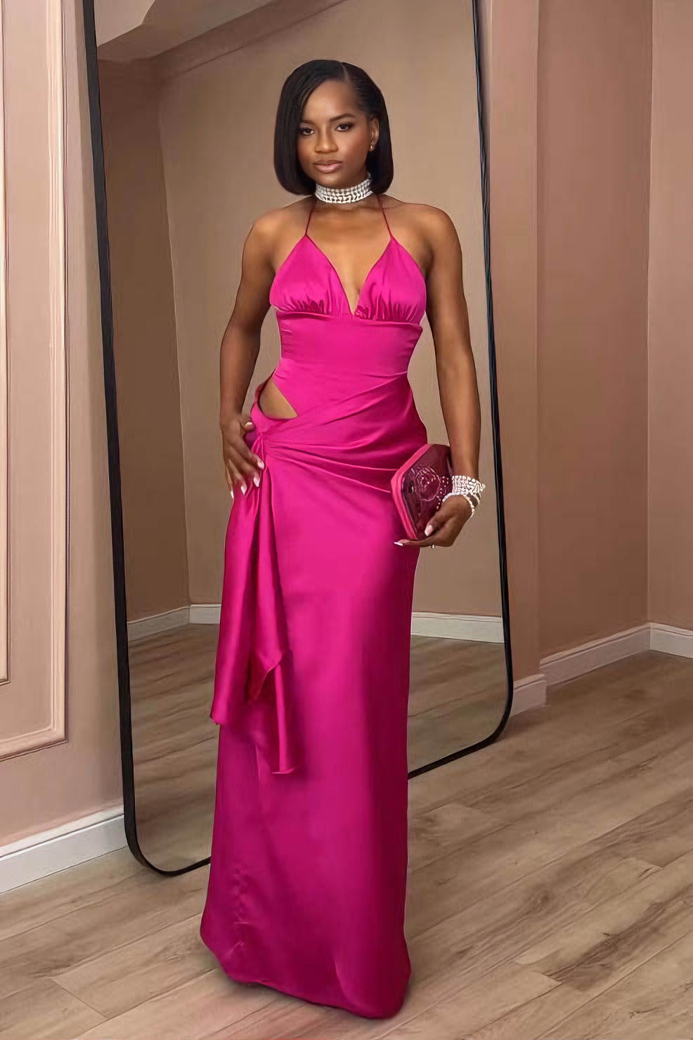 Pink - A woman modeling a formal, bright pink satin maxi gown featuring a halter neckline, a side cutout at the waist, and elegant draped detailing.