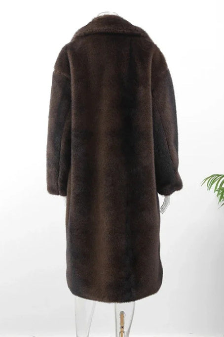 Brown - A woman wearing a long, oversized brown faux fur coat with a wide notch lapel, styled over a white shirt and jeans, standing in front of a dark SUV.