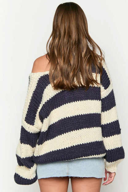 Black - Woman wearing a chunky knit, slouchy off-shoulder jumper featuring wide horizontal stripes, paired with light wash denim jeans.