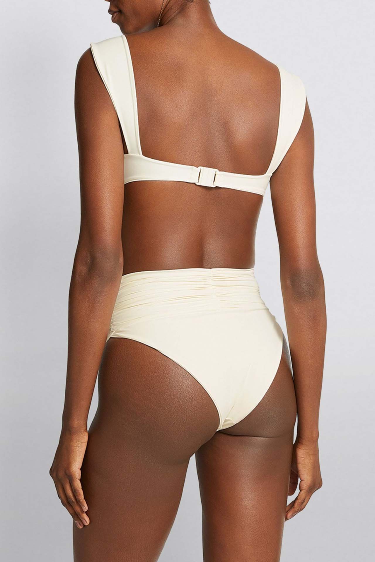 White - A woman models a structured, off-white two-piece bikini featuring a bandeau top with wide straps and high-waisted, high-cut bottoms adorned with a large, 3D rose appliqué at the waist.