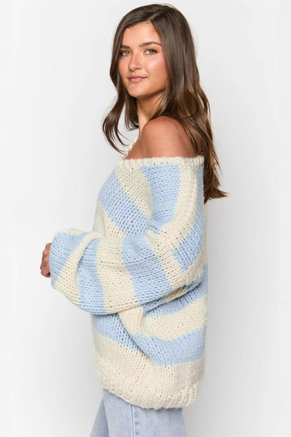 Blue - Woman wearing a chunky knit, slouchy off-shoulder jumper featuring wide horizontal stripes, paired with light wash denim jeans.