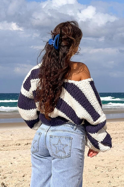 Black - Woman wearing a chunky knit, slouchy off-shoulder jumper featuring wide horizontal stripes, paired with light wash denim jeans.