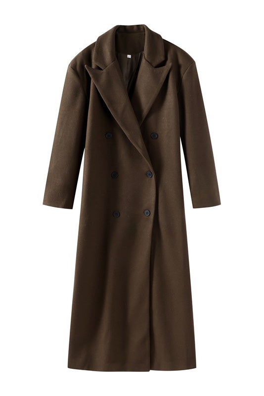 Brown - A woman wearing an oversized, dark brown double-breasted maxi coat with a notched lapel, styled over a beige sweater and light skirt.