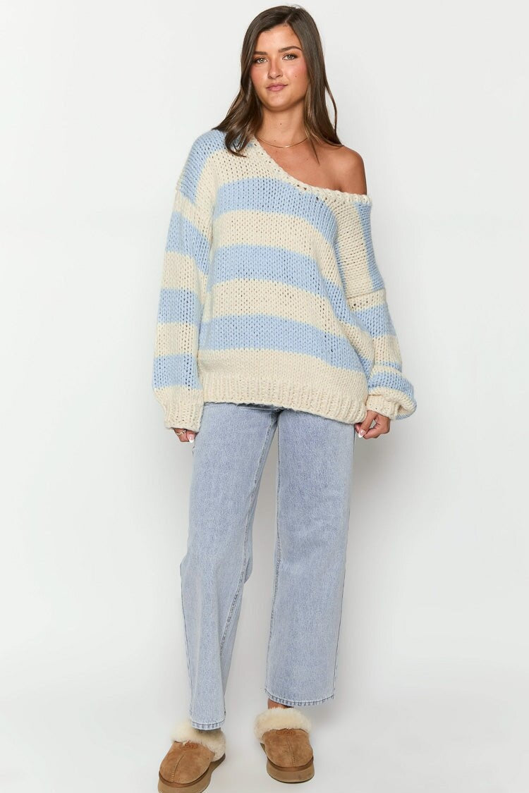 Blue - Woman wearing a chunky knit, slouchy off-shoulder jumper featuring wide horizontal stripes, paired with light wash denim jeans.