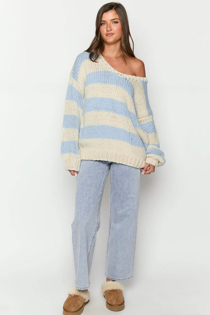 Blue - Woman wearing a chunky knit, slouchy off-shoulder jumper featuring wide horizontal stripes, paired with light wash denim jeans.