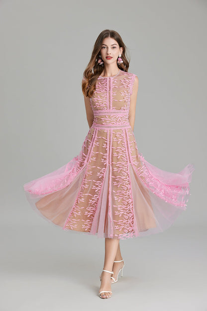Full-length view of a woman wearing a sleeveless, sheer midi dress in pink and nude, featuring elaborate pink botanical embroidery in vertical panels and a flared tulle skirt.