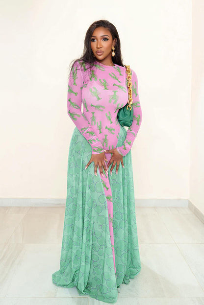 Woman in pink lobster print mesh dress with green flowing skirt and a green purse.