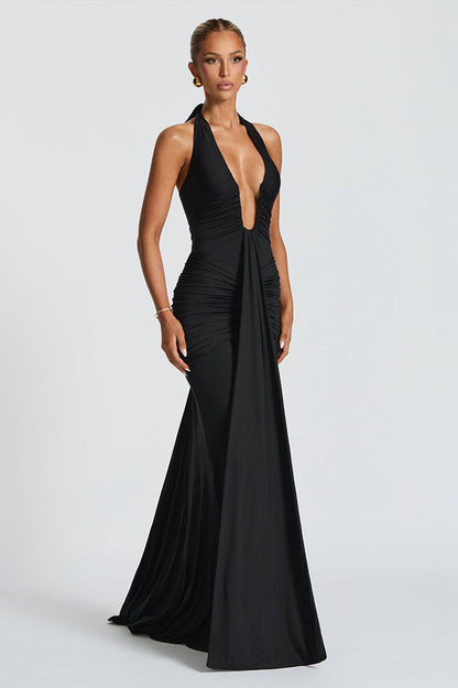 Black - A woman models a form-fitting, deep red halterneck maxi dress with a plunging neckline and extensive ruching, standing elegantly in a formal garden setting.