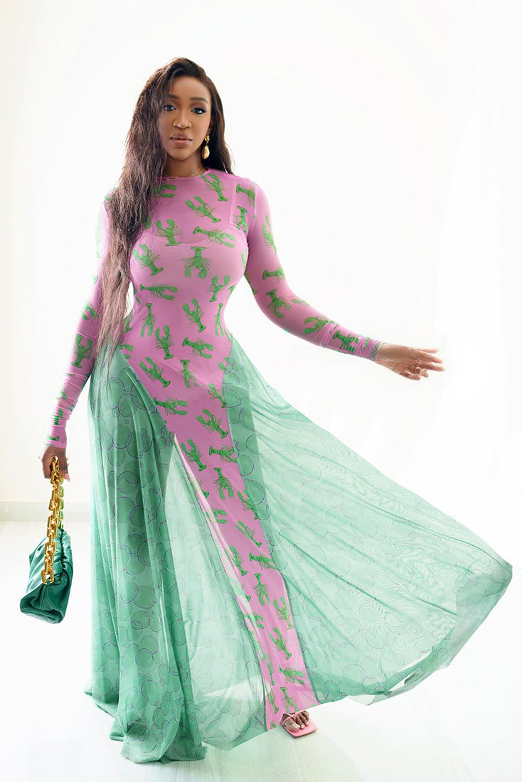 Woman in pink lobster print mesh dress with green flowing skirt and a green purse.