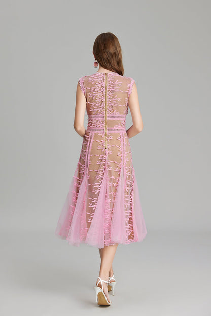 Full-length view of a woman wearing a sleeveless, sheer midi dress in pink and nude, featuring elaborate pink botanical embroidery in vertical panels and a flared tulle skirt.