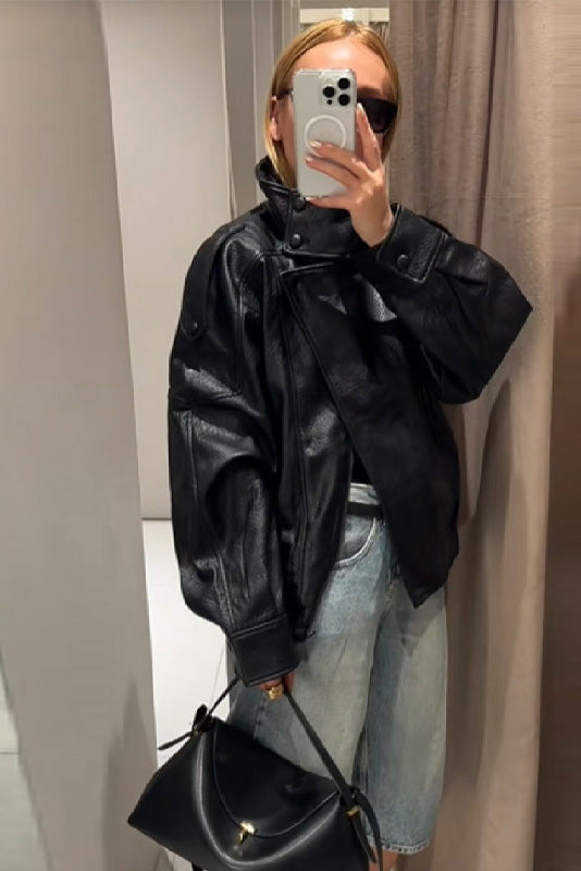 Black - A woman taking a mirror selfie wearing an oversized, black pebbled faux leather jacket with a high snap-button collar, dropped shoulders, and a cropped fit.