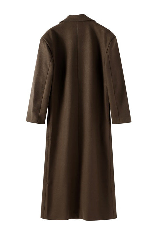 Brown - A woman wearing an oversized, dark brown double-breasted maxi coat with a notched lapel, styled over a beige sweater and light skirt.