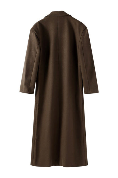 Brown - A woman wearing an oversized, dark brown double-breasted maxi coat with a notched lapel, styled over a beige sweater and light skirt.