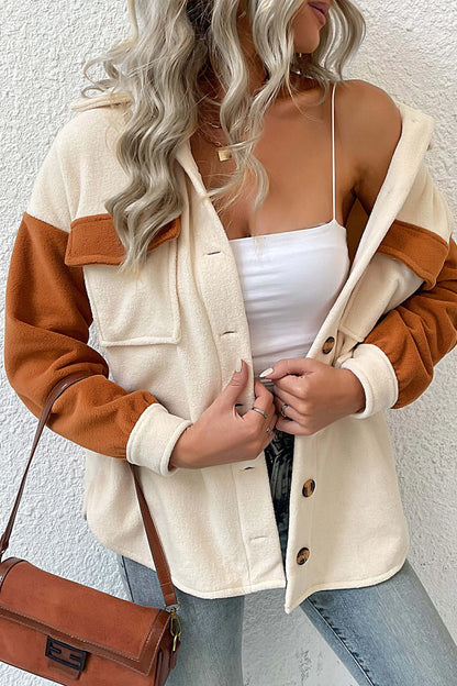 A woman wearing a relaxed fit, button-front shacket featuring a cream body with contrasting rust orange sleeves and chest pocket flaps, styled open over a white crop top and blue jeans.