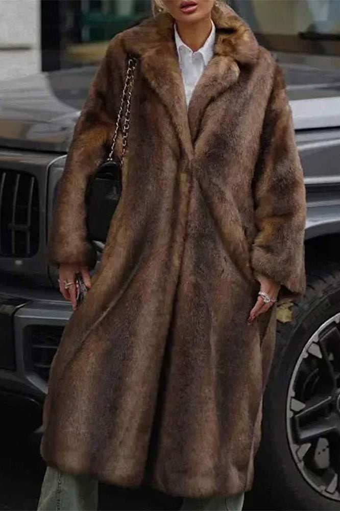 A woman modeling a long, heavyweight brown faux fur coat with a wide lapel collar, styled over a white collared shirt.