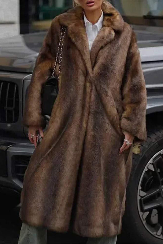 A woman modeling a long, heavyweight brown faux fur coat with a wide lapel collar, styled over a white collared shirt.