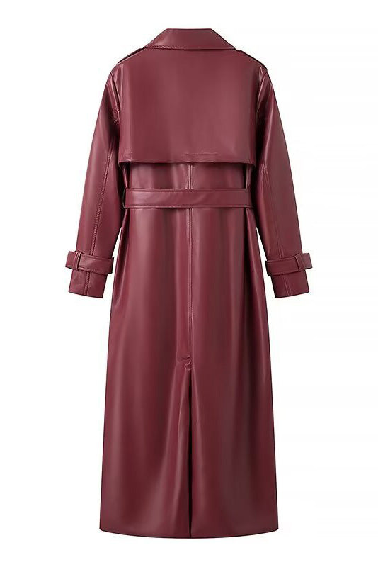 Red - A woman walking down a city street wearing a long, deep burgundy faux leather trench coat with a tie belt, styled over a black turtleneck and black leggings.
