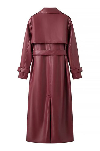 Red - A woman walking down a city street wearing a long, deep burgundy faux leather trench coat with a tie belt, styled over a black turtleneck and black leggings.