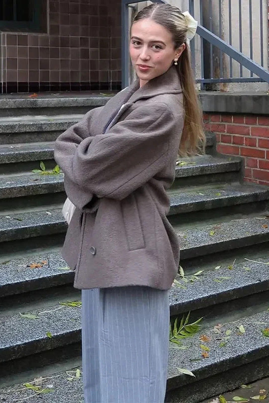 Grey - A woman wearing a taupe, short boxy jacket with oversized notch lapels, wide sleeves, and a double-breasted button front, styled over a black top.