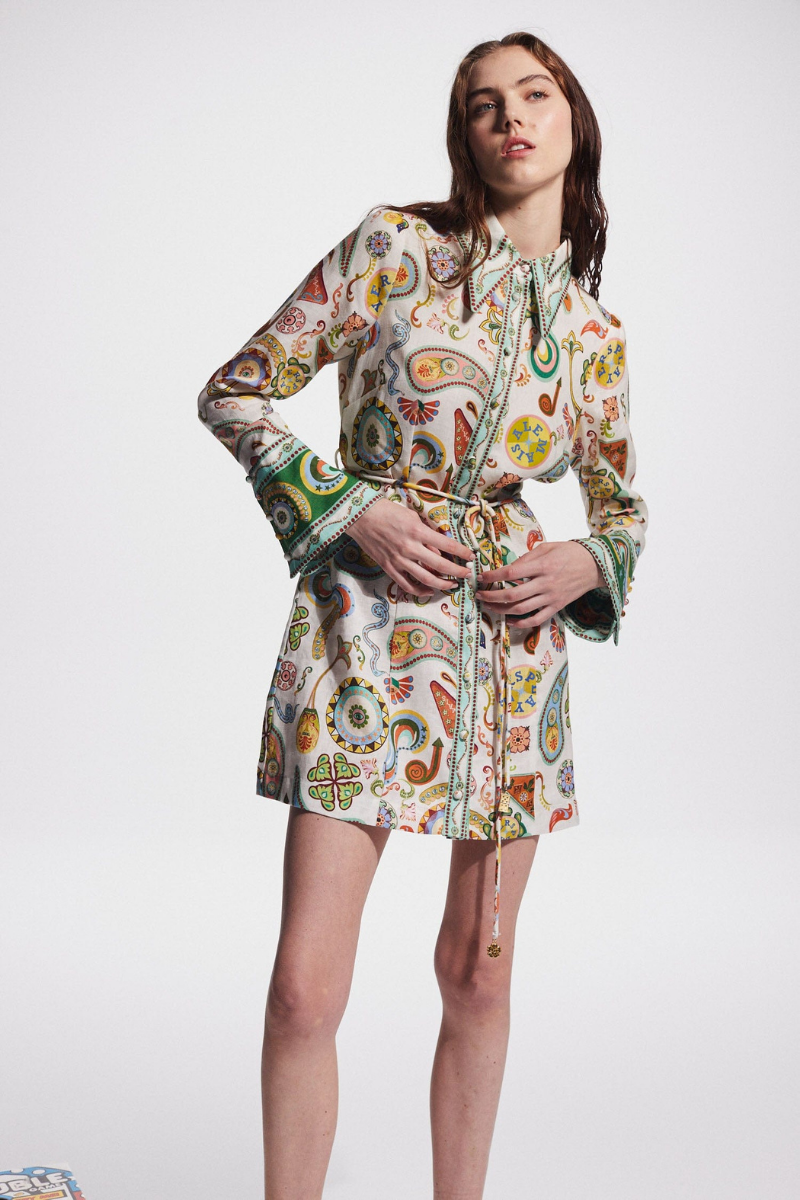 Multicolor - Full-length studio shot of a female model wearing a long-sleeved, collared mini shirt dress featuring a colourful paisley print, cinched at the waist with a tie-belt.