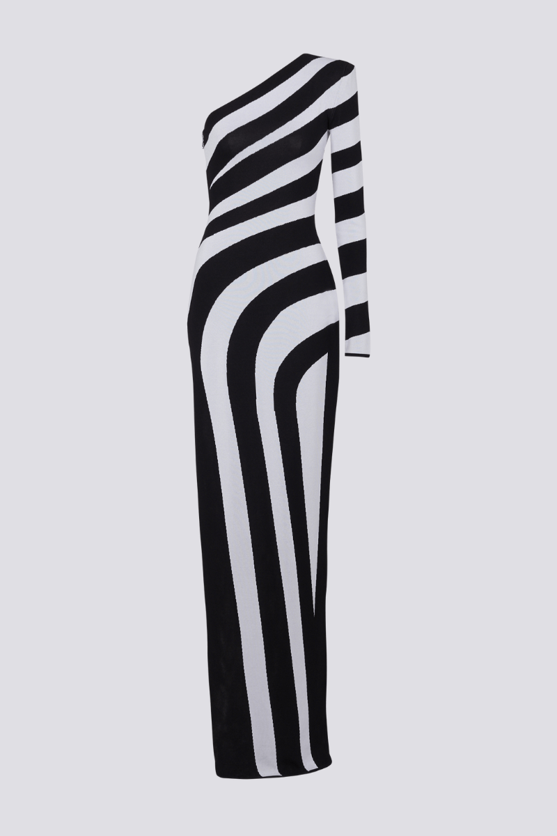 Black - A model stands in profile wearing a form-fitting, one-shoulder maxi dress with a single long sleeve, featuring a bold black and white diagonal stripe pattern and a high thigh slit.